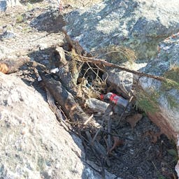 Photo of empty bottles in the remains of a a campfire between two rocks.